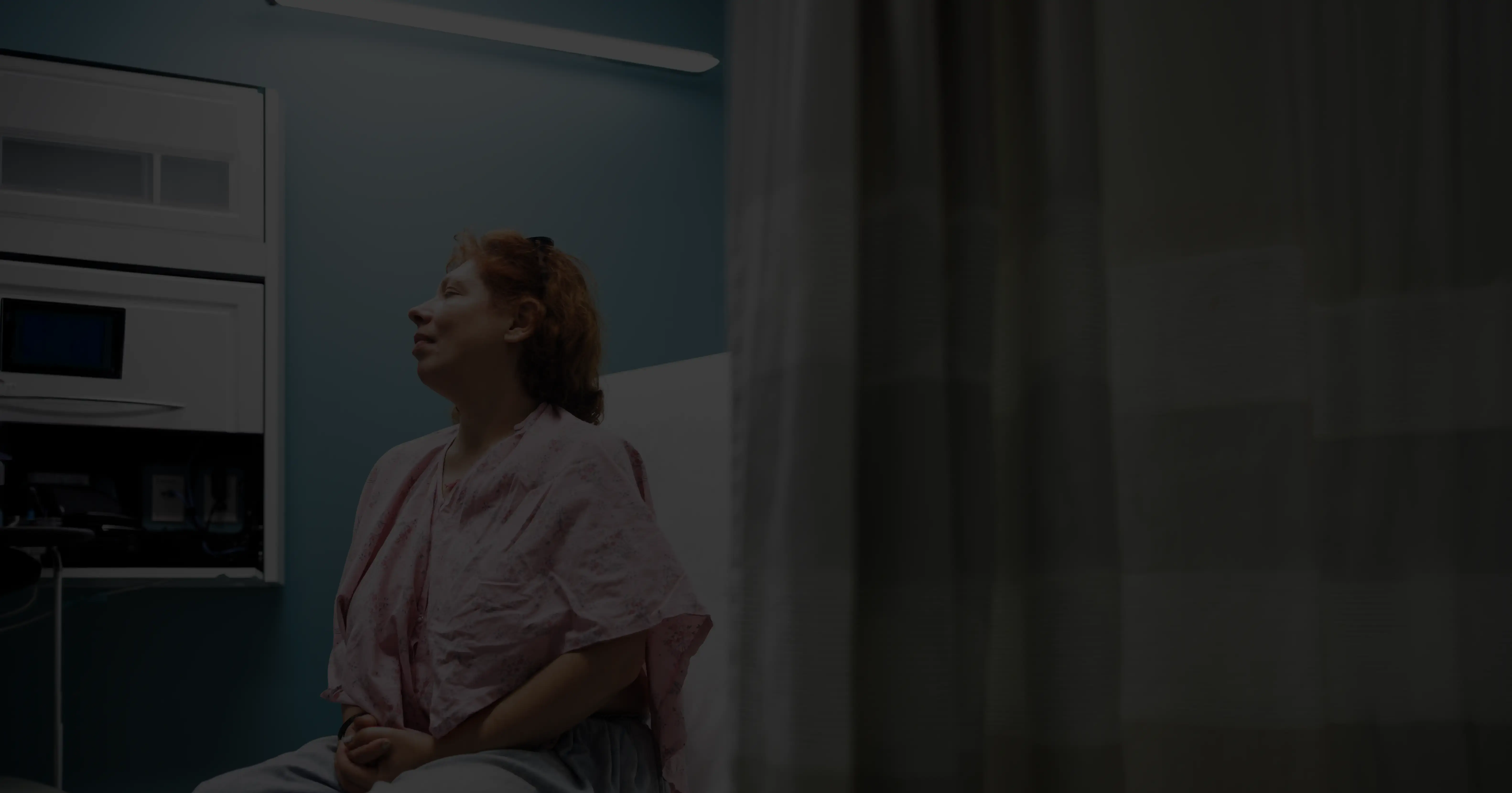 a photograph of a patient in a pink medical gown sitting on a clinic examination table