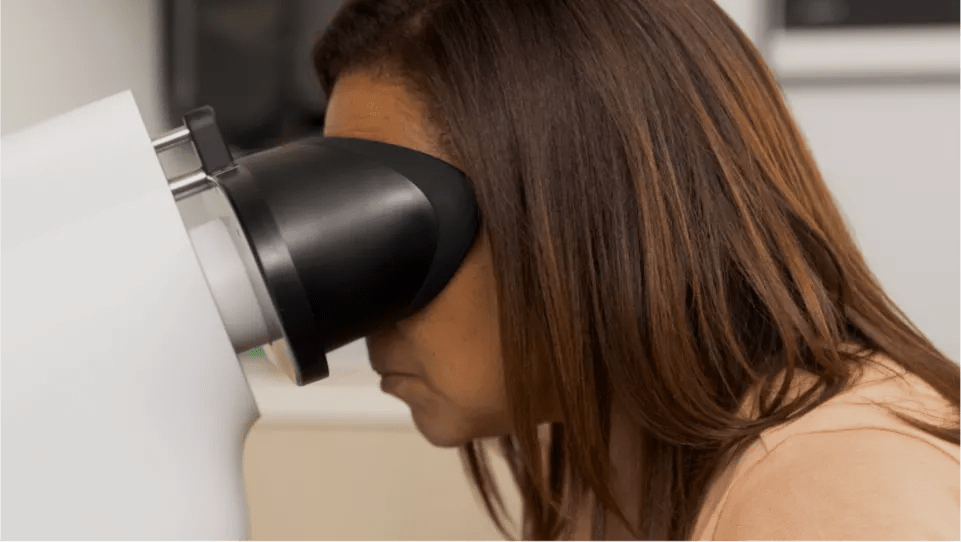Close-up of a woman leaning into a Verily retinal camera with her head resting on the headrest, which covers her eyes.