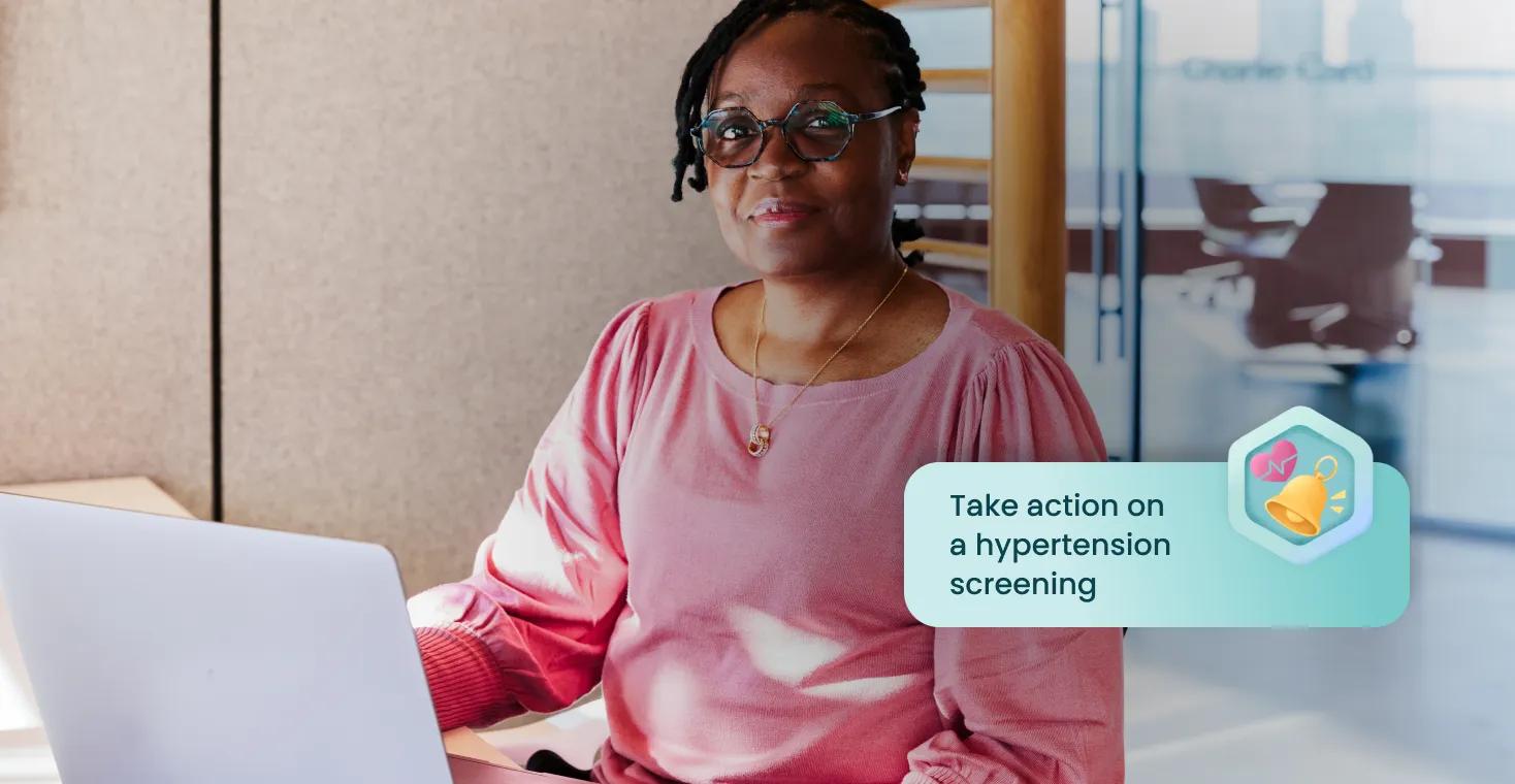 Care team member sits at a computer next to a Verily Me notification that says, “Take action on a hypertension screening”