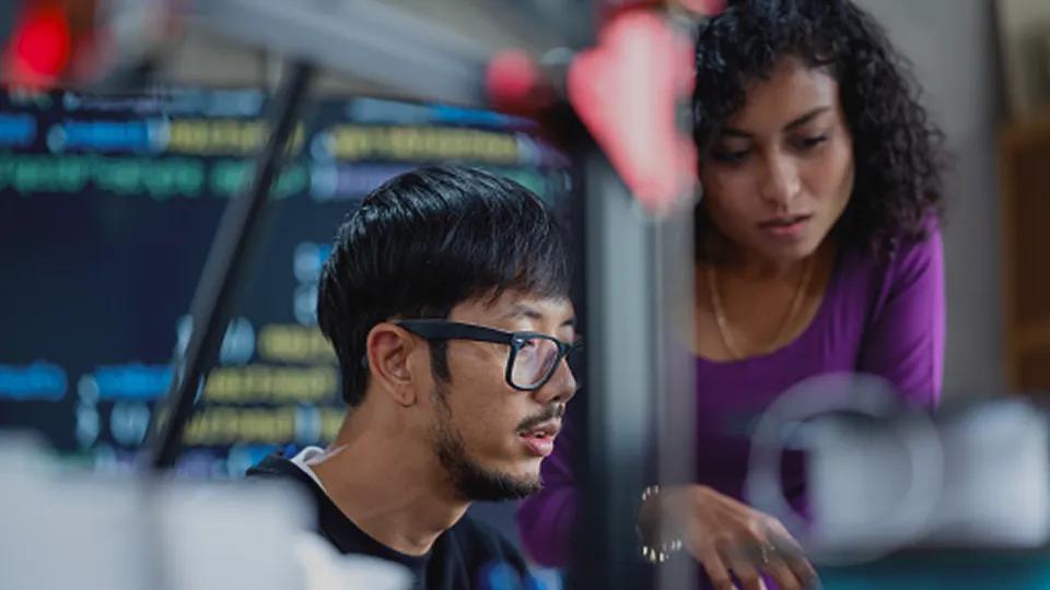 Researcher sitting at a computer wearing protective goggles and gloves looking at a screen 