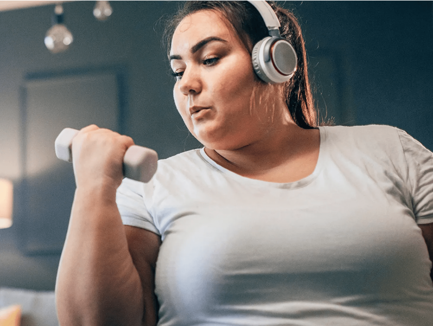 An obese woman in her early thirties doing bicep curls at home with water nearby. She’s sticking to the convenient activity plan she created with her virtual program care team.