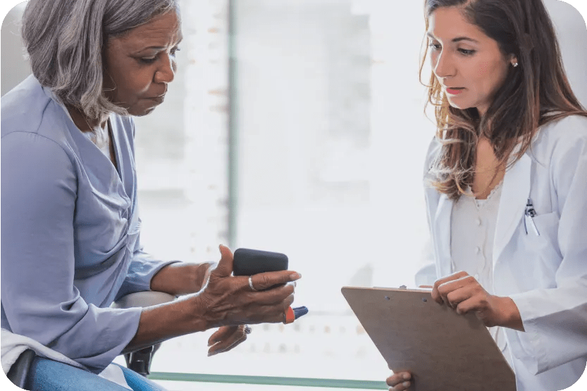 A woman shows something on her phone to a clinician with a clipboard