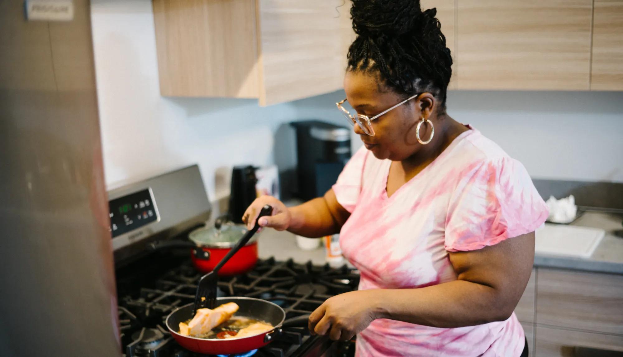 Woman preparing a healthy salmon dish in her kitchen while filming the N of 1 episode.