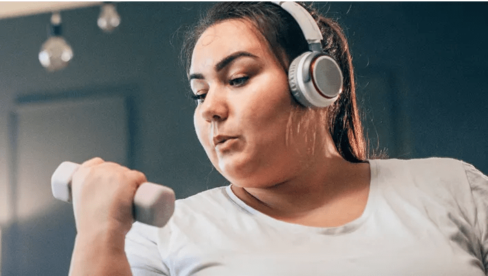 An obese woman in her early thirties doing bicep curls at home with water nearby. She’s sticking to the convenient activity plan she created with her virtual program care team.