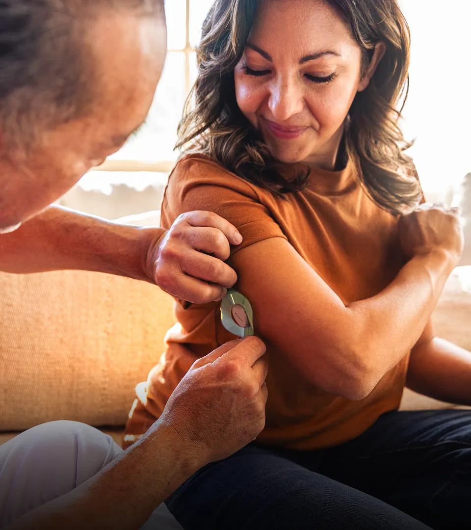 A hispanic woman in her late forties, having a CGM device applied to her arm as part of her Verily care program.